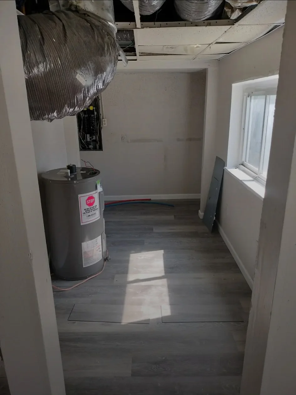 Utility area during finish work with new resilient flooring installed around the water-heater and service area.